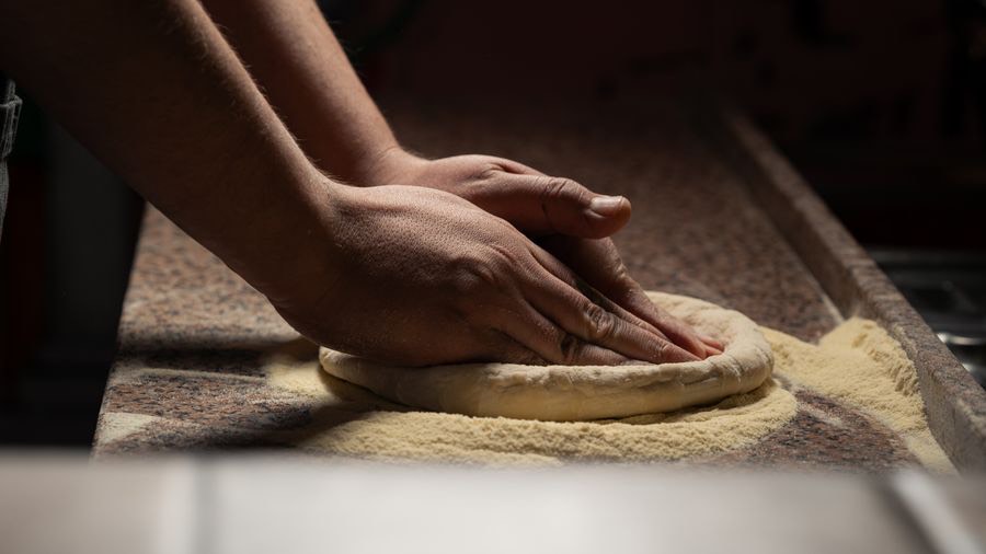 Hände formen Pizzateig auf bemehlter Arbeitsfläche